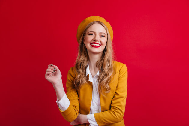 女性幸福的法国女模特在笑红墙上孤立的戴贝雷帽的金发女孩的正面图享受积极手势