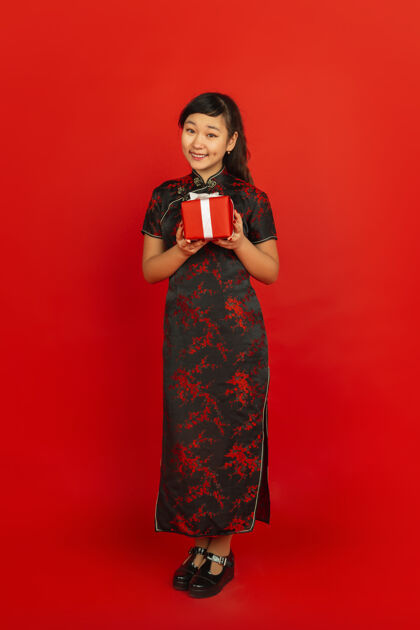 新中国新年红色背景上孤立的亚洲少女肖像身着传统服装的女模特看起来很开心 微笑着展示礼盒庆祝 节日 情感普通话年欢乐
