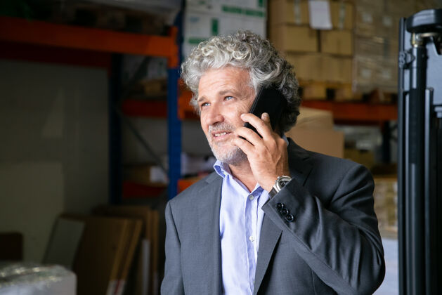 仓库沉思积极的成熟企业家站在仓库里用手机说话背景是货架上的商品复制空间商业或通讯概念成熟站立物流