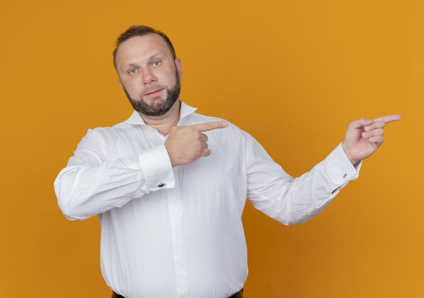 看一个留着胡子的男人穿着白衬衫 手指着站在橙色墙上的一边指指点点壁板穿