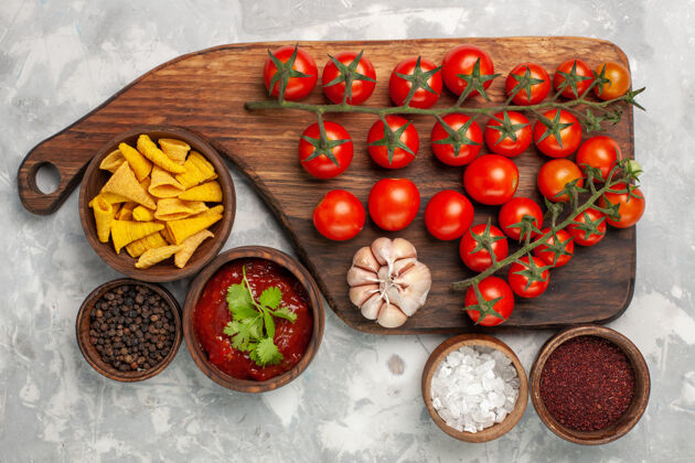 不同顶视新鲜樱桃番茄与不同的调味品在白色表面调味品膳食生的