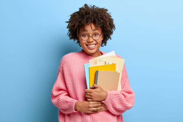 年轻一个穿着粉色毛衣的非洲裔微笑女人记事本学习微笑
