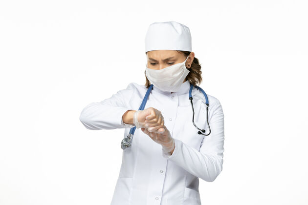 正面正面图年轻女医生戴着无菌口罩和手套由于白色表面有冠状病毒医生专业手套