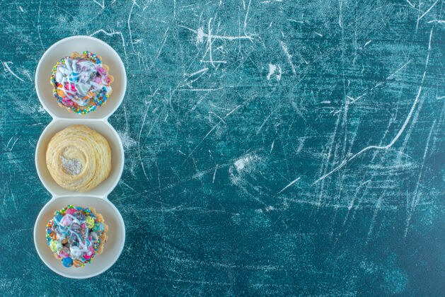 甜食蓝色背景的小盘子里放着饼干和纸杯蛋糕高质量的照片糖果烘焙曲奇