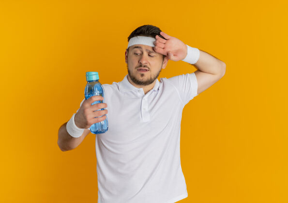 累了身穿白衬衫 头箍 手拿一瓶水的年轻健身男子站在橙色背景下 显得疲惫不堪站着抱着男人