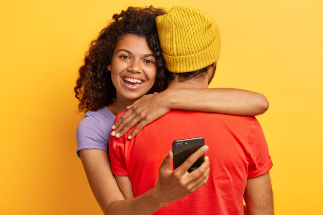 看快乐的美国黑人女子拥抱男友 手持手机 时刻保持联系 很高兴见到朋友 表达爱意和关怀的水平镜头不要脸的男子退后 接受拥抱年轻人种族