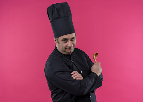 站着男厨师身穿黑色制服 头戴厨师帽 手持木勺 站在粉色背景下 自信地看着镜头厨师黑色勺子