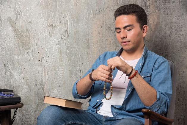 电话年轻人戴上手镯 坐在椅子上 把书放在大理石背景上高质量的照片男人年轻人人