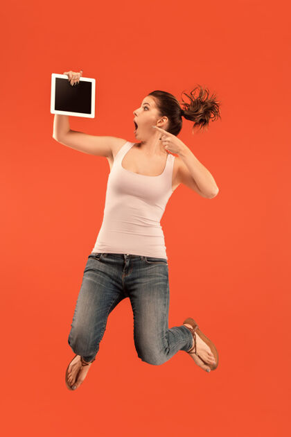 博客使用笔记本电脑或平板电脑小玩意在蓝色工作室背景上跳跃的年轻女子在运动或运动中奔跑的女孩人类情感和面部表情概念现代生活中的小玩意无线跳跃人