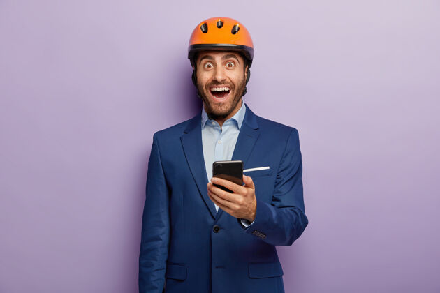 电子快乐工程师的形象手持手机 给同事发短信 戴着橙色头盔 穿着优雅西装工业穿着人