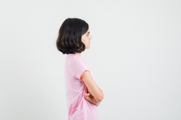 休闲小女孩交叉着双臂站在粉色t恤里 看起来很专注和平好看年轻