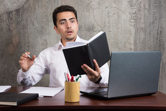 桌子震惊的员工看着笔记本 坐在办公桌前高质量的照片男书笔记本电脑