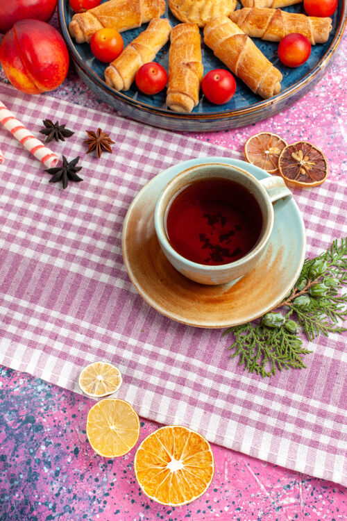 茶顶视图甜美美味的百吉饼在托盘内与李子新鲜桃子和一杯茶在淡粉色的桌子上美味里面糖