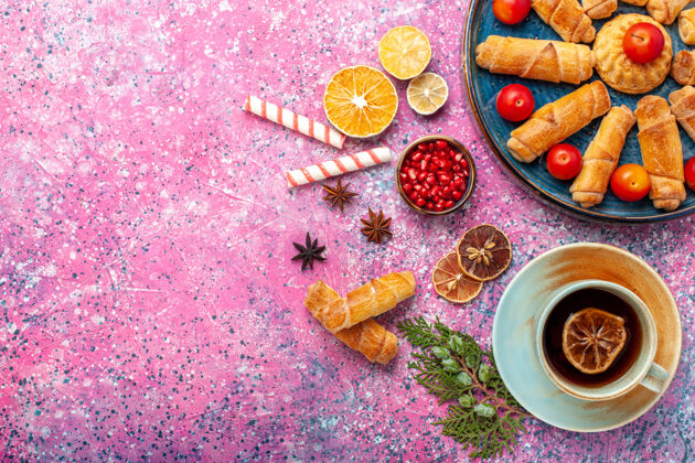 茶顶视图甜美美味的百吉饼内托盘与李子和茶杯的粉红色表面生的百吉饼五颜六色