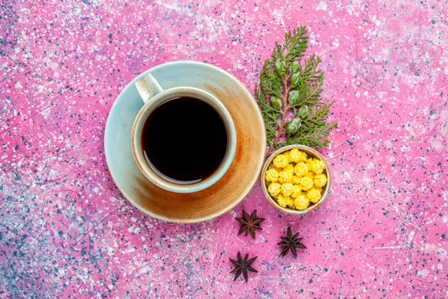 糖粉红色书桌上的一杯茶和黄色糖果茶碟饮料甜食