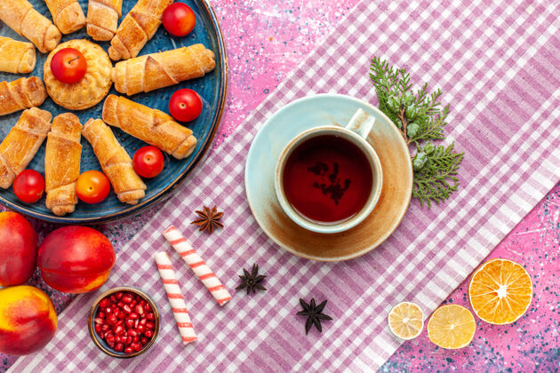 托盘顶视图甜美美味的百吉饼在托盘内与李子新鲜桃子和一杯茶在淡粉色的桌子上桌子新鲜派