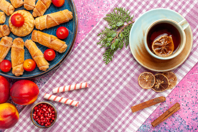 食物顶视图甜甜可口的百吉饼在托盘里与李子桃子和茶杯在淡粉色的桌子上饼干顶部托盘