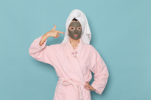 男人正面图：年轻女性 穿着粉色浴袍 淋浴后 脸上戴着深色面罩 蓝色墙壁上 美丽的水霜 自我护理淋浴浴室年轻人女人后面