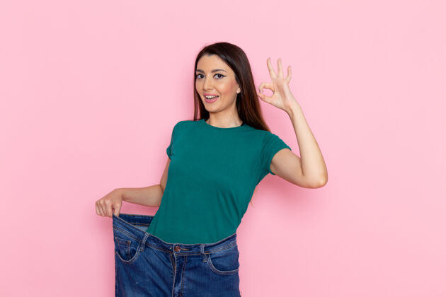 年轻正面图身着绿色t恤的年轻女性在粉色墙壁上展示她苗条的身体腰部运动锻炼美丽苗条的运动员腰部显示女性