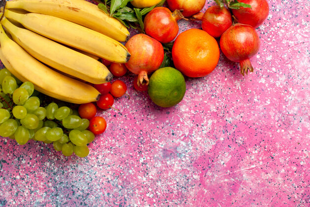 生的顶视黄色新鲜香蕉美味的水果与葡萄和石榴在粉红色的办公桌上苹果异国情调办公桌