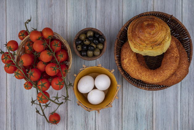 木材在灰色木质背景上 新鲜橄榄放在木碗上 葡萄藤西红柿放在桶上 面包放在篮子里顶部食物藤蔓