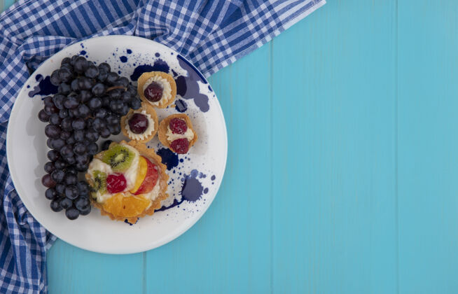 食物水果纸杯蛋糕和葡萄的顶视图在蓝色背景上的格子布上 有复制空间复制格子衣服