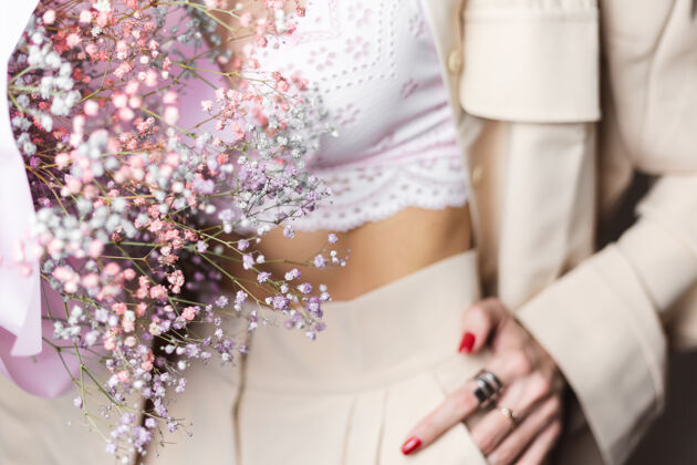 性感近景：穿着米色西装和白色胸罩的无头女人手拿一束五颜六色的干花 手上戴着两个戒指配饰女人闪亮