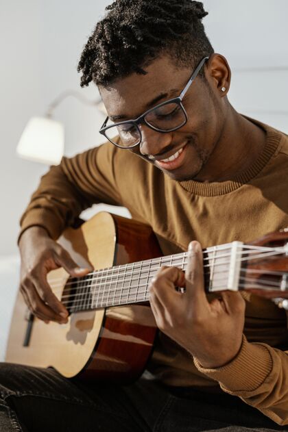 乐器笑脸男音乐家在家的前视图在床上弹吉他男性技能创造者