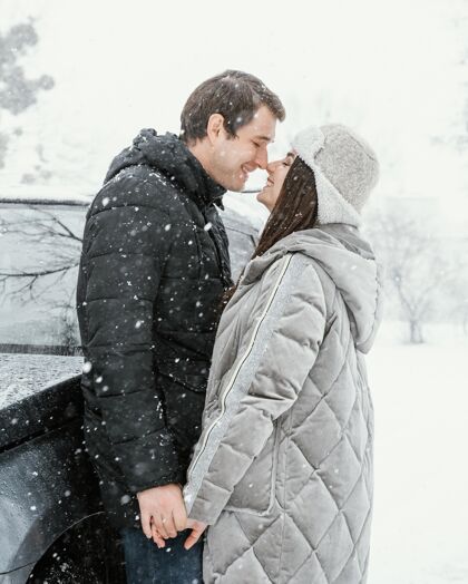 冬天侧视图笑脸夫妇亲吻在雪中 而在公路旅行女性接吻户外