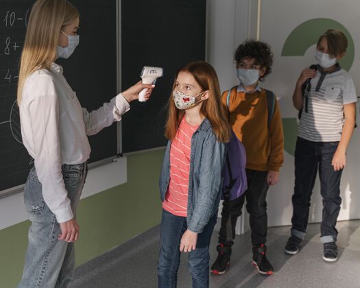 孩子带着医用面罩的女老师在学校检查孩子们的体温女性数码学习