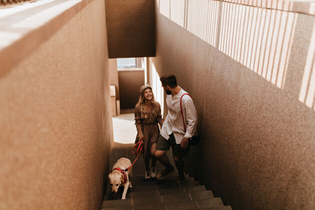 棕色连衣裙戴着帽子 穿着棕色裙子的快乐女孩和她的男朋友微笑着走上楼梯 打算遛狗朋友微笑男性