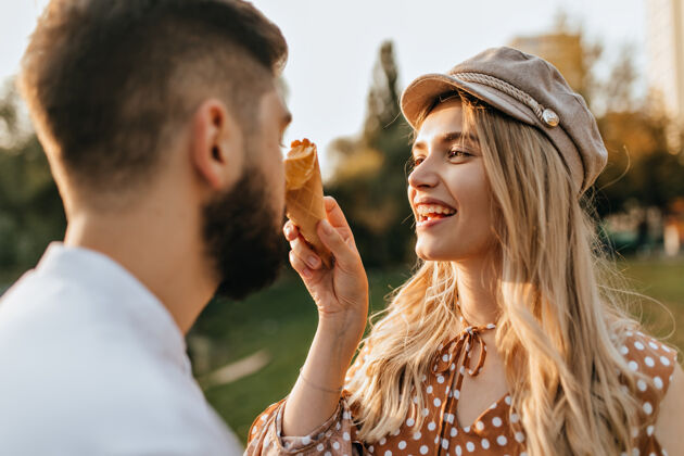 自然戴着时髦帽子和圆点上衣的开朗女士笑着 用甜瓜冰淇淋涂抹着丈夫的鼻子成人户外散步