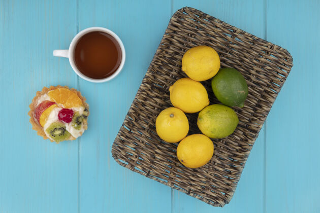 茶一桶新鲜柠檬的顶视图 蓝色木质背景上有一杯茶和水果馅饼木头景观酸