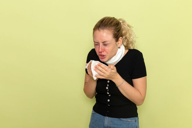 视图正面图：年轻女性 喉咙周围缠着白毛巾 感觉非常不舒服 打喷嚏在浅绿色的墙上生病生病的女性健康女孩打喷嚏感觉病人