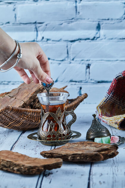 芳香女人的手拿着一勺茶和各种糖果放在蓝色的木桌上地毯热的饼干