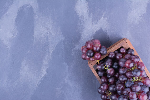 产品红葡萄放在蓝色表面的木制托盘里多汁蔬菜美味