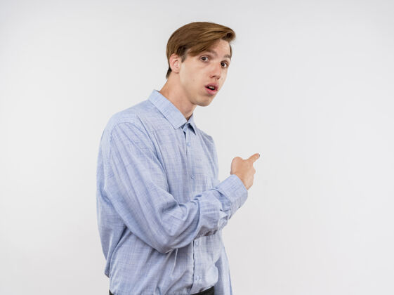 惊喜穿蓝色衬衫的年轻人用食指指着站在白墙上的某个看起来很惊讶的东西站着男人目录