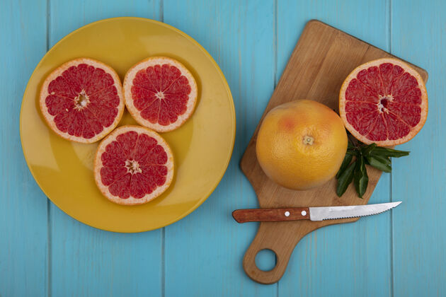 刀用刀和楔子在绿松石背景上的黄色盘子上的砧板上俯视葡萄柚葡萄柚楔形黄色
