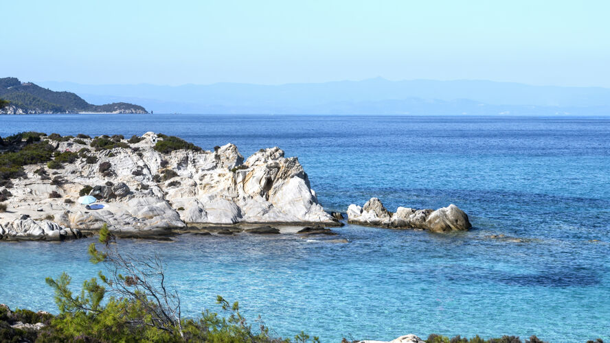 海岸线爱琴海海岸周围绿树成荫 岩石和灌木丛 蓝色的海水和休息的人 希腊悬崖希腊海岸