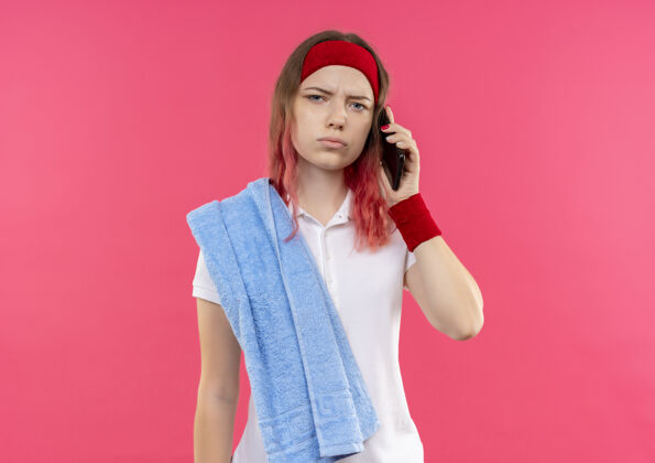 站戴着头巾 肩上扛着毛巾 站在粉红色的墙上 一脸困惑和焦急地讲着电话的年轻运动女郎女人年轻市民