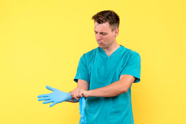 人黄色墙上戴着手套的男医生的正视图男性医院情绪