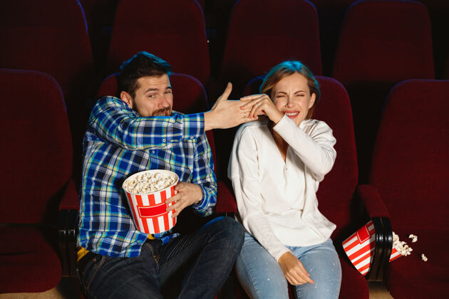 爆米花迷人的年轻白种人夫妇在电影院 房子或电影院看电影看起来富于表现力 惊讶和情绪化独自坐着玩关系 爱情 家庭 周末时间生活方式害怕娱乐