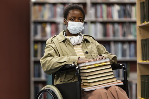 年轻轮椅上戴着口罩的女孩手里拿着一堆书Campus生活方式大学