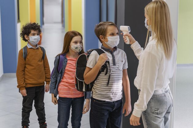 课堂戴着医用面罩的女老师在学校检查孩子体温的侧视图学生知识流行病