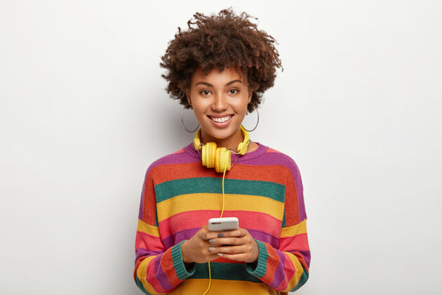 牙齿快乐的非洲裔美国少女拿着手机连着耳机灵感女性高兴