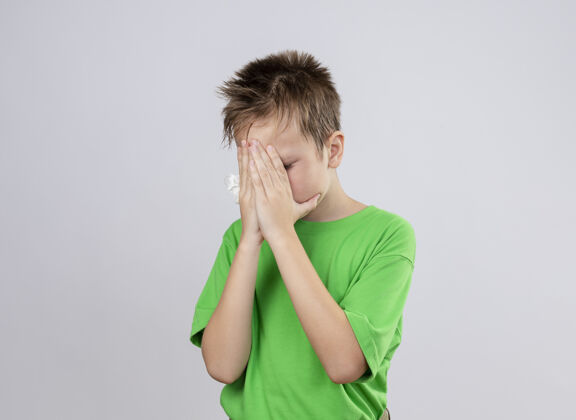 脸生病的小男孩穿着绿色t恤 感觉不舒服 用手捂着脸站在白墙上疾病不适男孩