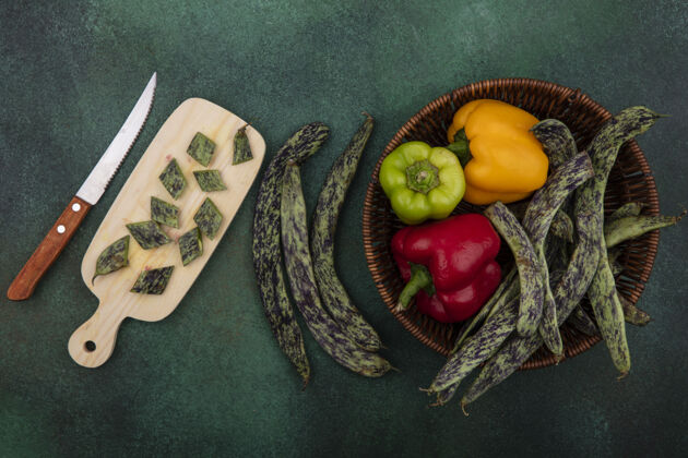 刀顶视图绿豆和甜椒放在一个篮子里 菜板上有一把刀 背景是绿色的观点新鲜顶部