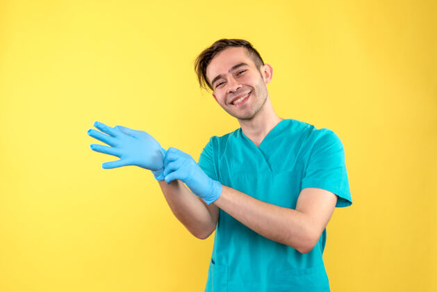 健康黄色墙上戴着蓝色手套的男医生的正视图休闲医疗男人