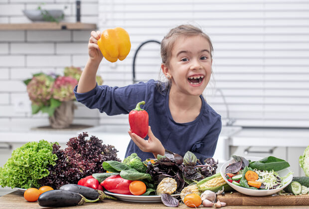 饮食快乐的小女孩拿着甜椒背景上的各种蔬菜健康食品的概念可爱素食主义者食物