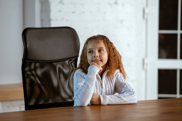 孩子穿着休闲服的年轻白人女孩的肖像看起来梦幻 可爱 快乐抬头思考 坐在室内的木桌旁未来的概念 目标 梦想 想象人类爱完美